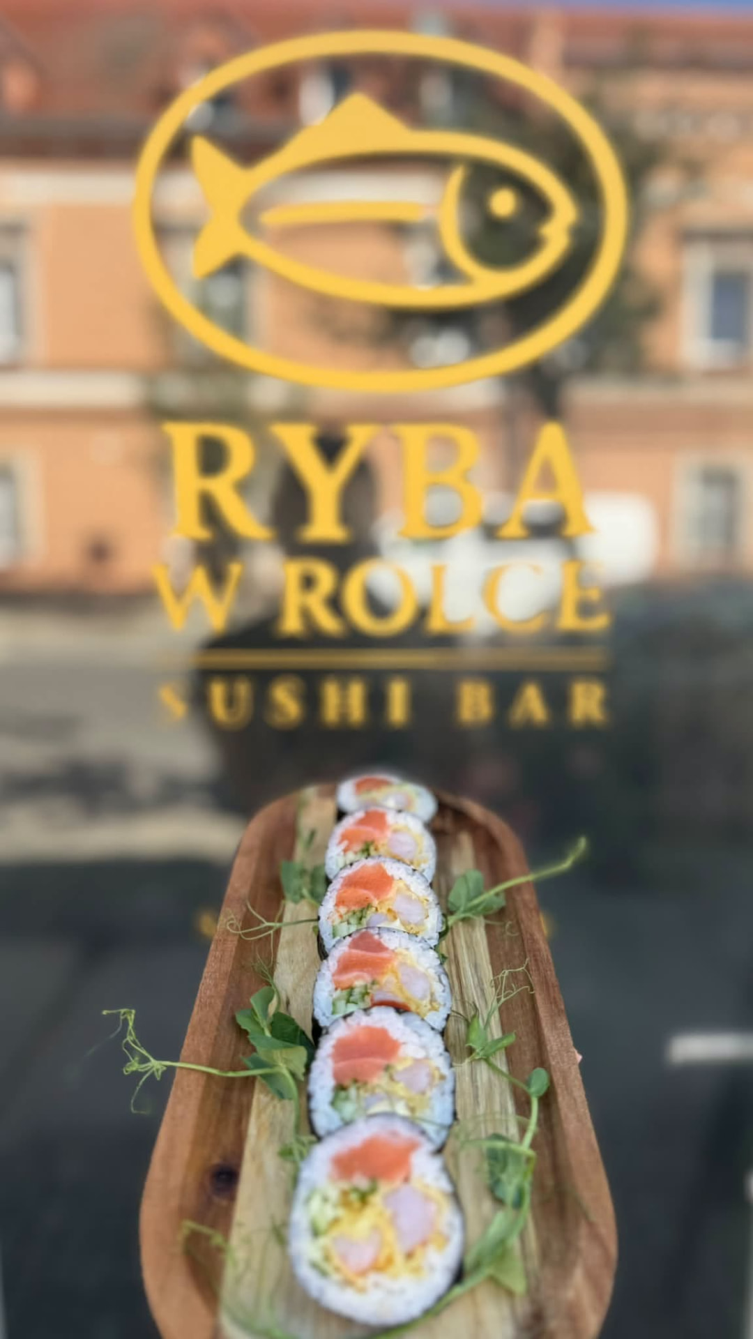 Futomaki z łososiem i krewetką na tle logo Ryba w Rolce Sushi Bar na witrynie